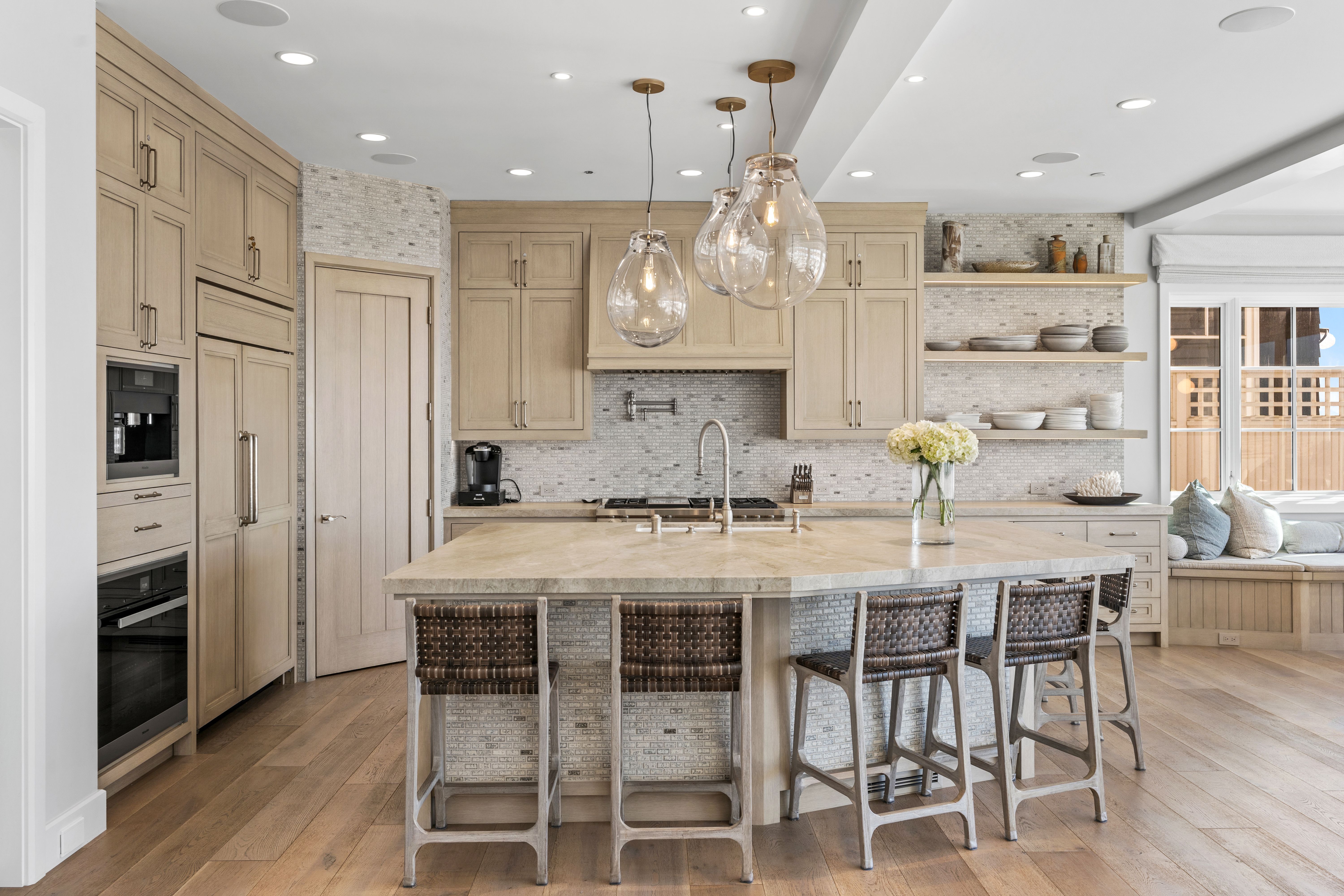 Warm-toned kitchen with wood cabinetry, a stone island, woven barstools, and glass pendant lighting