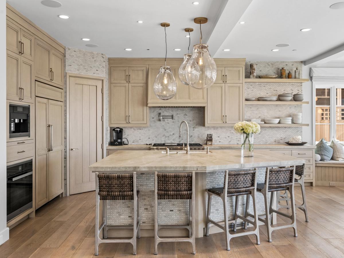 Warm-toned kitchen with wood cabinetry, a stone island, woven barstools, and glass pendant lighting