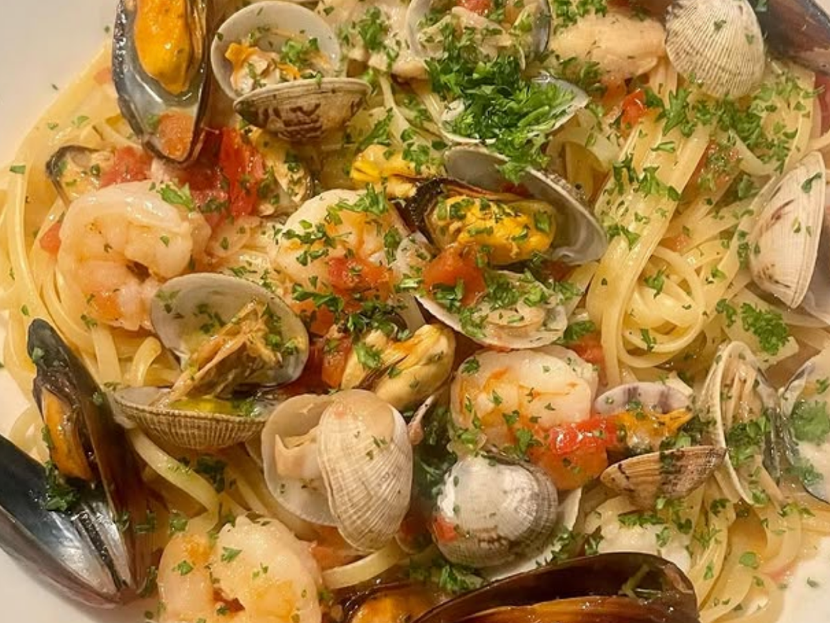 Plate of linguine pasta topped with shrimp, mussels, clams, diced tomatoes, and fresh parsley