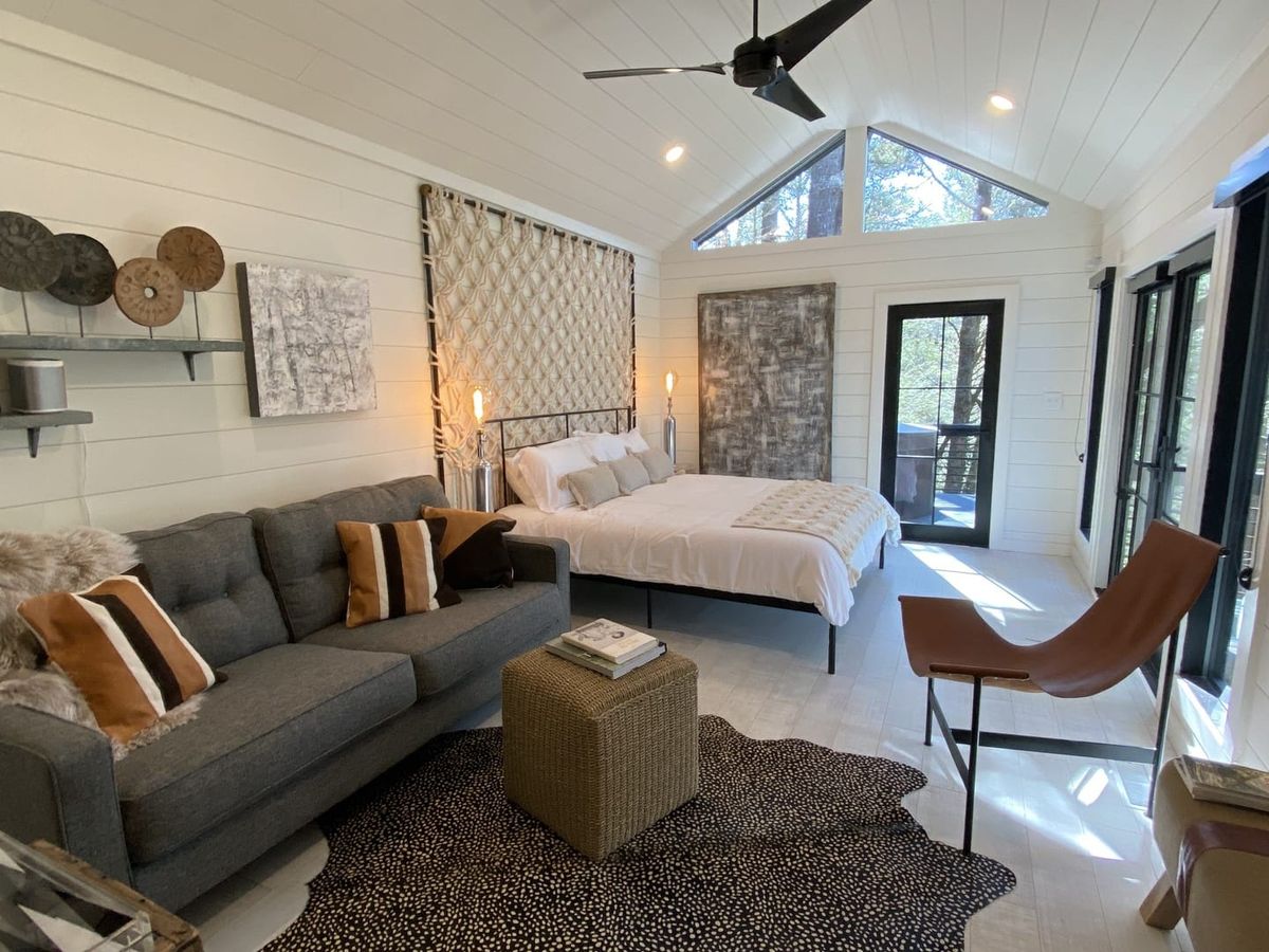 This cozy A-frame cabin suite features a king bed, modern decor, and a private deck. Big windows let in sunlight and views of the trees all around.