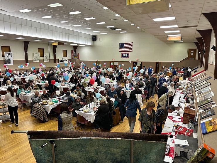 Dozens of people fill a decorated hall with balloons and dinner tables to celebrate the Buffalo Bill Birthday Ball. Guests chat, eat, and bid in silent auctions under the American flag, honoring Cody’s beloved Western legacy.