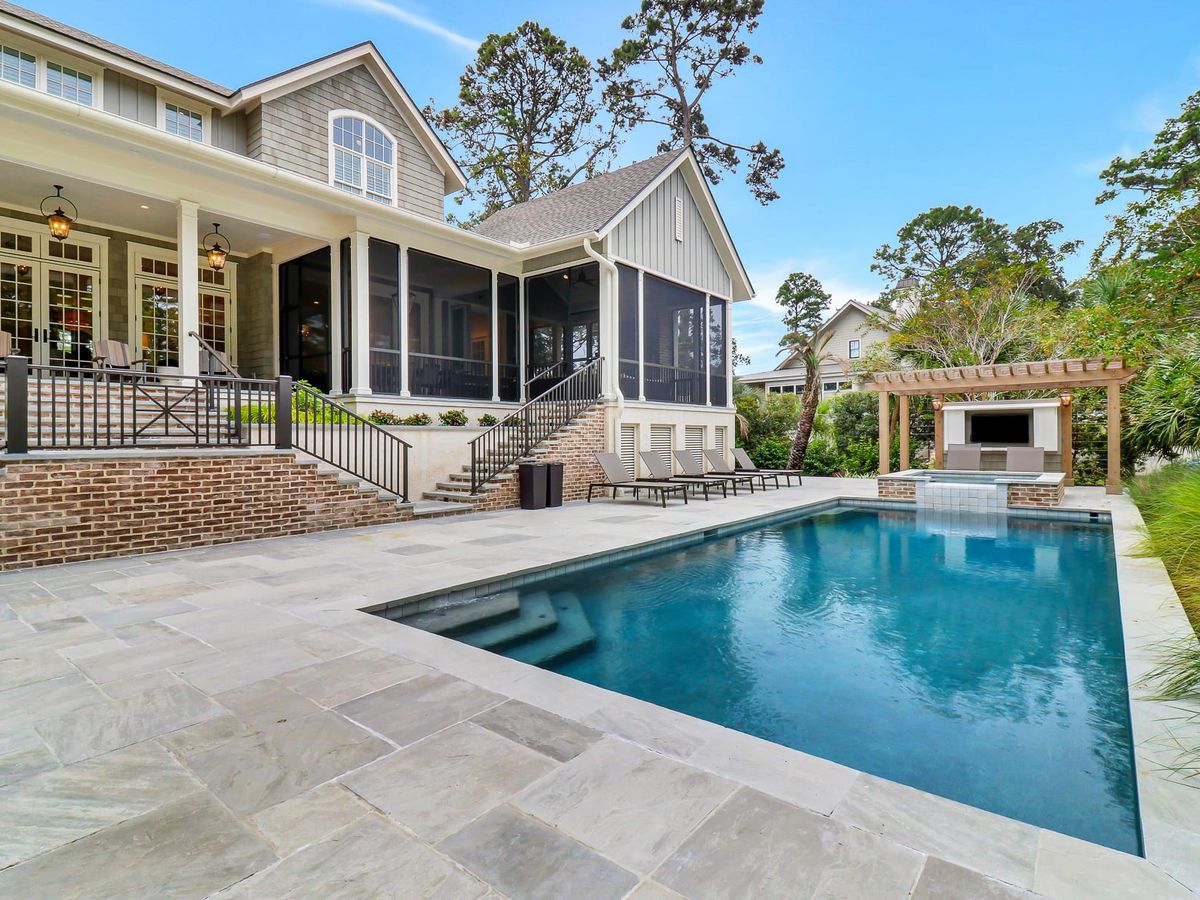 A casually elegant new-construction home features an expansive open layout with custom decor, exceptional artwork, and seamless indoor-outdoor living, including a heatable pool and spa, a screened porch with a gas log fireplace, and a separat