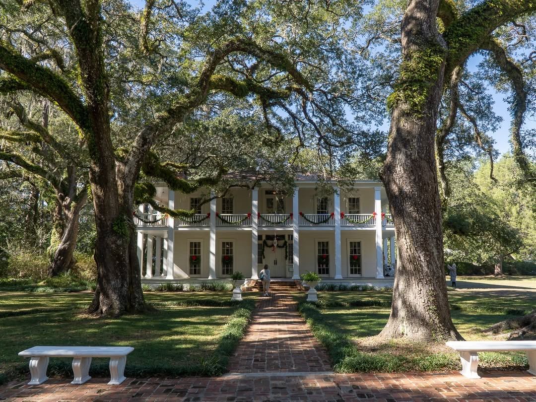 The historic Wesley House at Eden Gardens State Park, framed by moss-draped oak trees and a brick pathway leading to its white columns. A scenic spot full of charm and Southern history.
