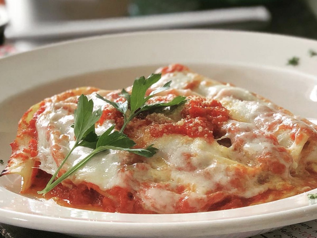 A serving of cheesy baked lasagna topped with marinara sauce, grated parmesan, and fresh parsley, presented on a white plate.