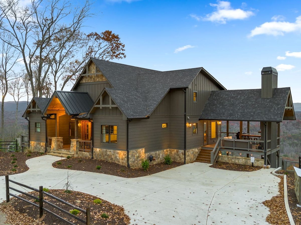 Blue Run Cabin features a modern mountain design with dark wood siding, stone accents, and panoramic views. The large driveway and cozy porch welcome you into a peaceful retreat in the hills.