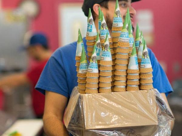 Inside Ben & Jerry’s iconic factory, a cheerful employee carries a box stacked with colorful ice cream cones, ready for another busy day of tours and tastings. The playful atmosphere captures the fun, quirky spirit that made this Vermont-born brand famous worldwide.
