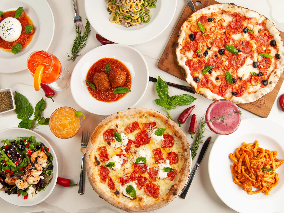 A vibrant Italian feast at Pomo with Neapolitan pizzas, pasta, salads, and colorful cocktails. The authentic presentation captures the essence of traditional Italian dining.