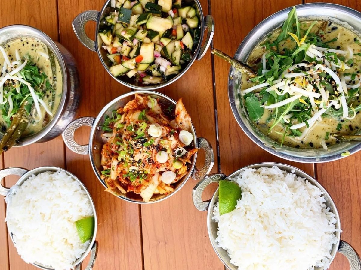 Colorful spread of global-inspired dishes including creamy green curry, fresh cucumber salad, spicy kimchi, and fluffy white rice.