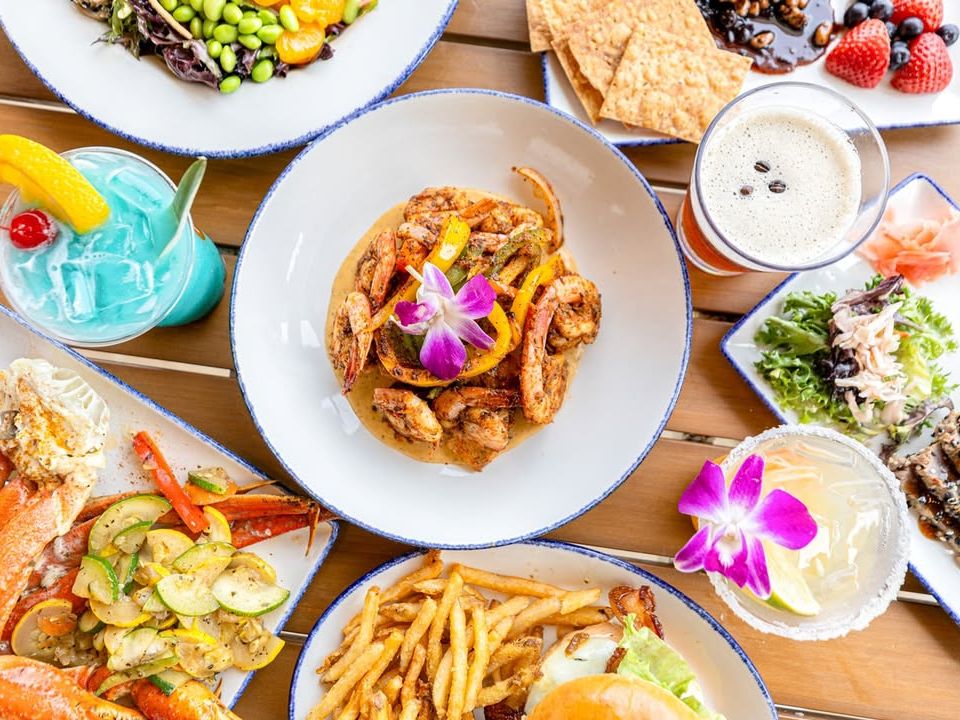 A colorful spread of seafood, tropical drinks, shrimp, crab legs, fries, and sushi—topped with edible flowers. A beachside feast that’s perfect for sunny days and fun vibes.