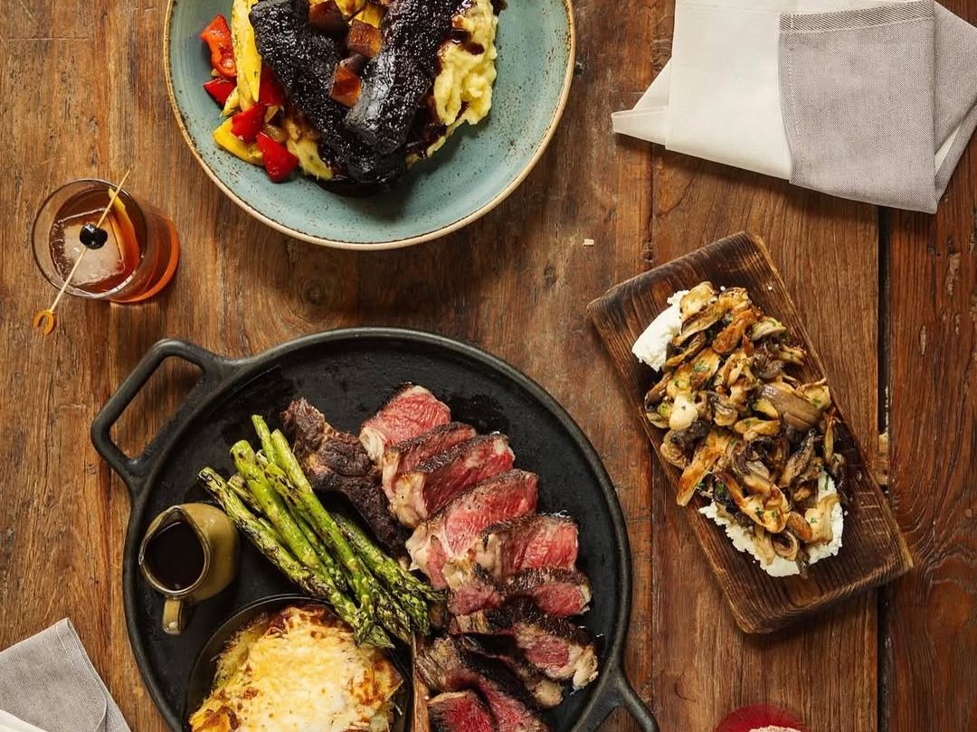 A rustic Montana feast at Horn & Cantle with grilled steak, asparagus, braised short ribs, and hearty sides. One of Big Sky’s must-try fine dining spots serving bold western flavors.