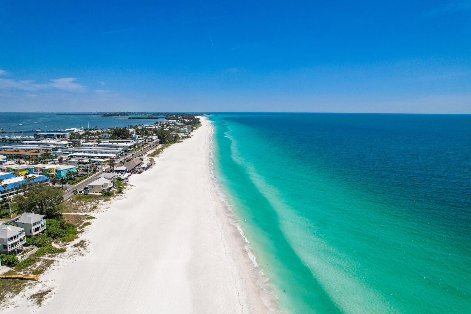 A stunning aerial view of Anna Maria Island and Sarasota shows soft white sand beaches and bright turquoise water stretching along the coast. You can see beach homes and a long shoreline that makes this area perfect for relaxing beach walks and sunny Florida vacations.