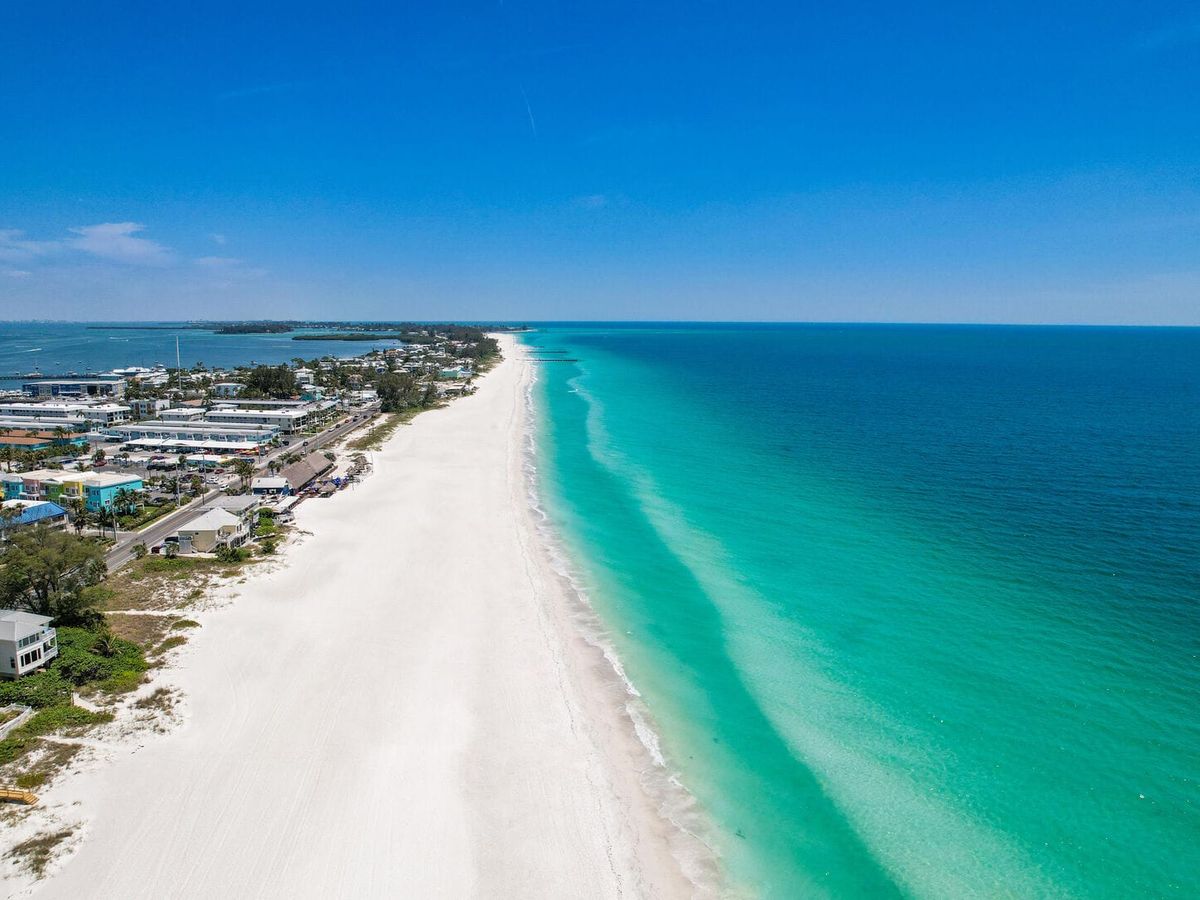 A stunning aerial view of Anna Maria Island and Sarasota shows soft white sand beaches and bright turquoise water stretching along the coast. You can see beach homes and a long shoreline that makes this area perfect for relaxing beach walks and sunny Florida vacations.