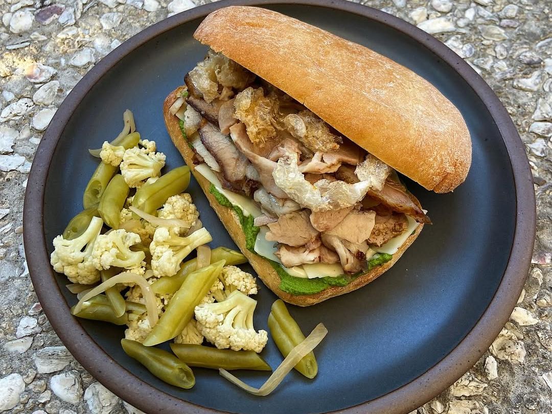 A toasted ciabatta sandwich stuffed with pork, cheese, and crispy bits, served with house-pickled veggies. A must-try rustic bite with bold flavors.