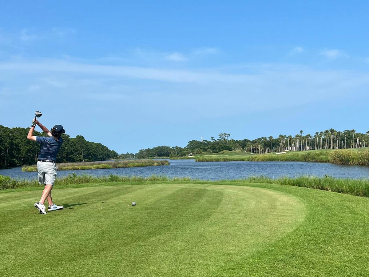 Guy on golf course swinging his golf club with lake in foreground