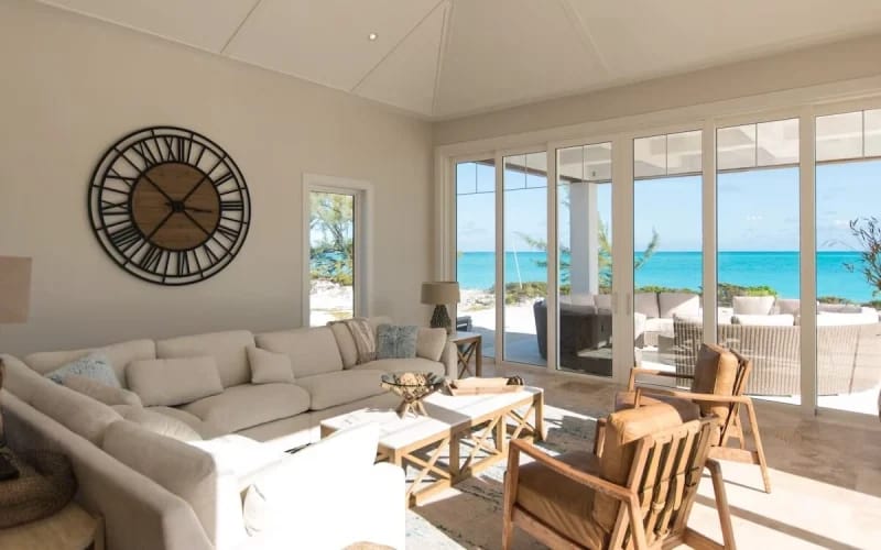 An airy oceanfront living space in The Bahamas with floor-to-ceiling windows framing turquoise sea views. Neutral tones, soft sunlight, and cozy furnishings create a calm island retreat for family and friends.
