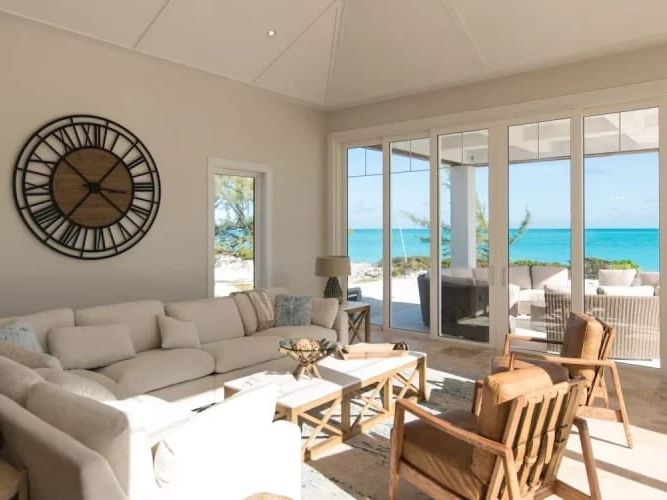 An airy oceanfront living space in The Bahamas with floor-to-ceiling windows framing turquoise sea views. Neutral tones, soft sunlight, and cozy furnishings create a calm island retreat for family and friends.