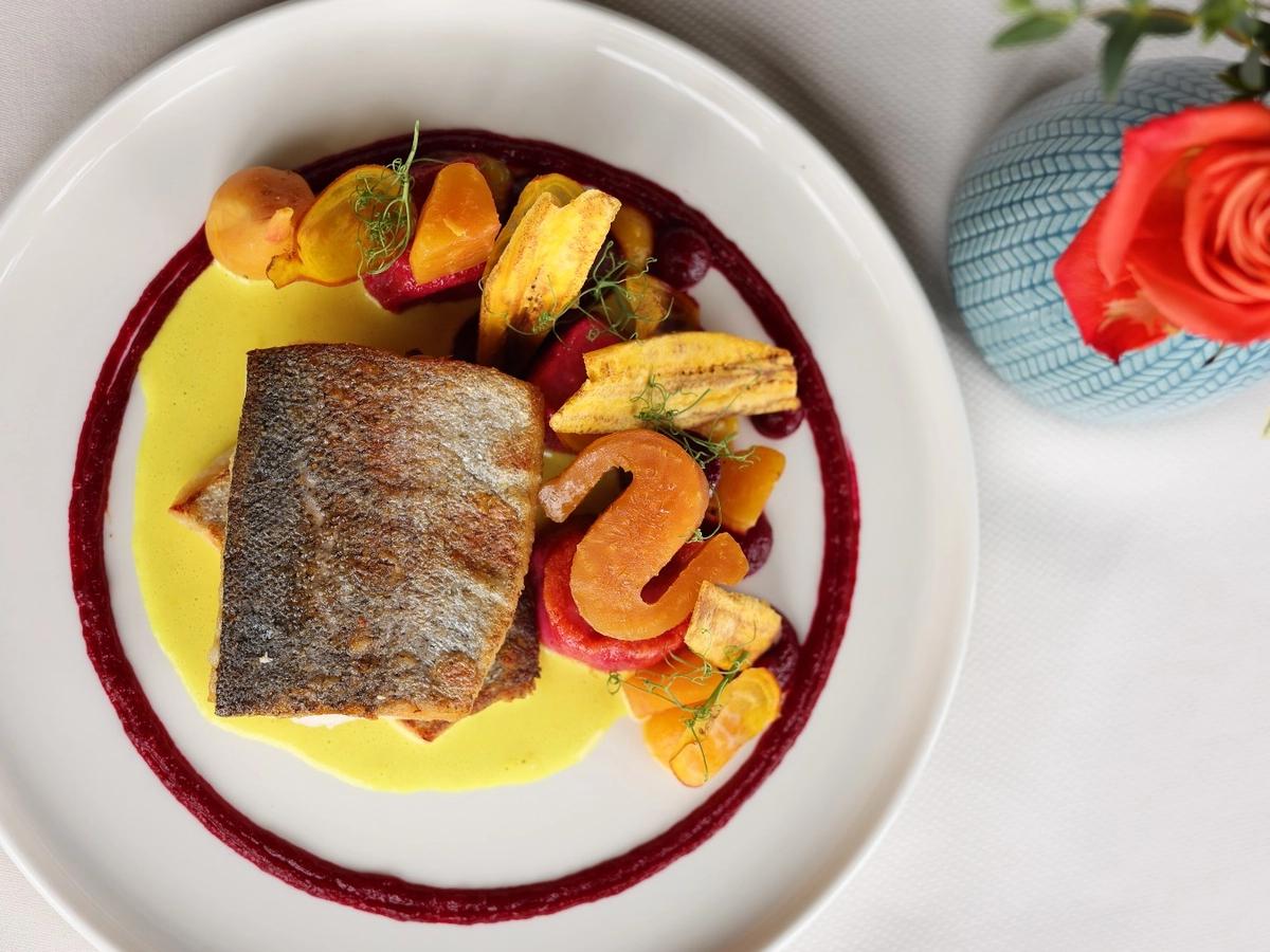 A beautifully plated seafood dish at Jasmine Porch, featuring fresh fish with colorful vegetables and rich sauce. This fine dining restaurant is known for creative Southern flavors and elegant presentation.