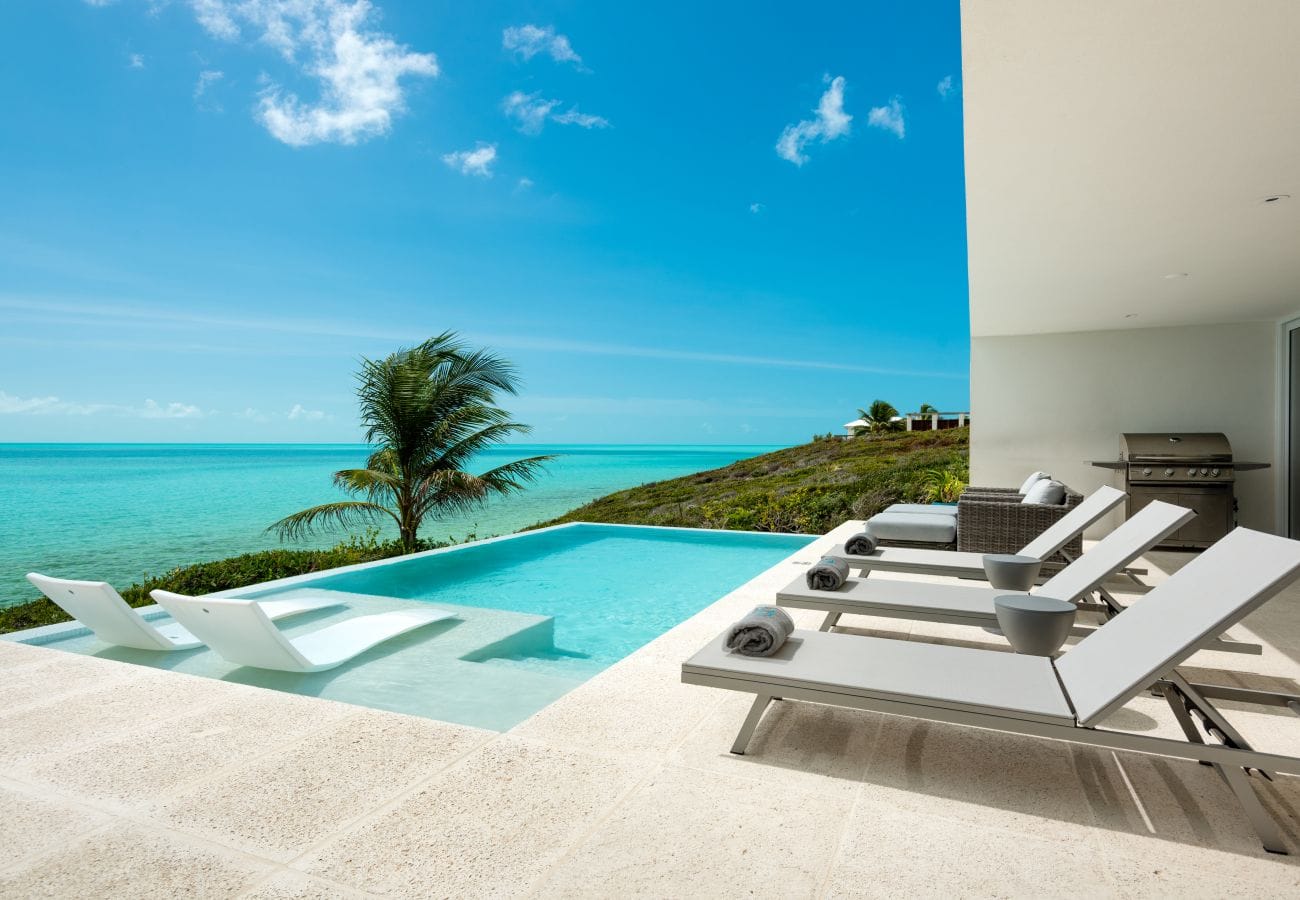 This oceanfront pool deck sits right above bright turquoise water, offering a quiet and dreamy place to relax under the sun. Sleek loungers and a modern design make the space feel clean, calm, and luxurious. It’s the kind of vacation spot that feels almost unreal in how beautiful and peaceful it is.