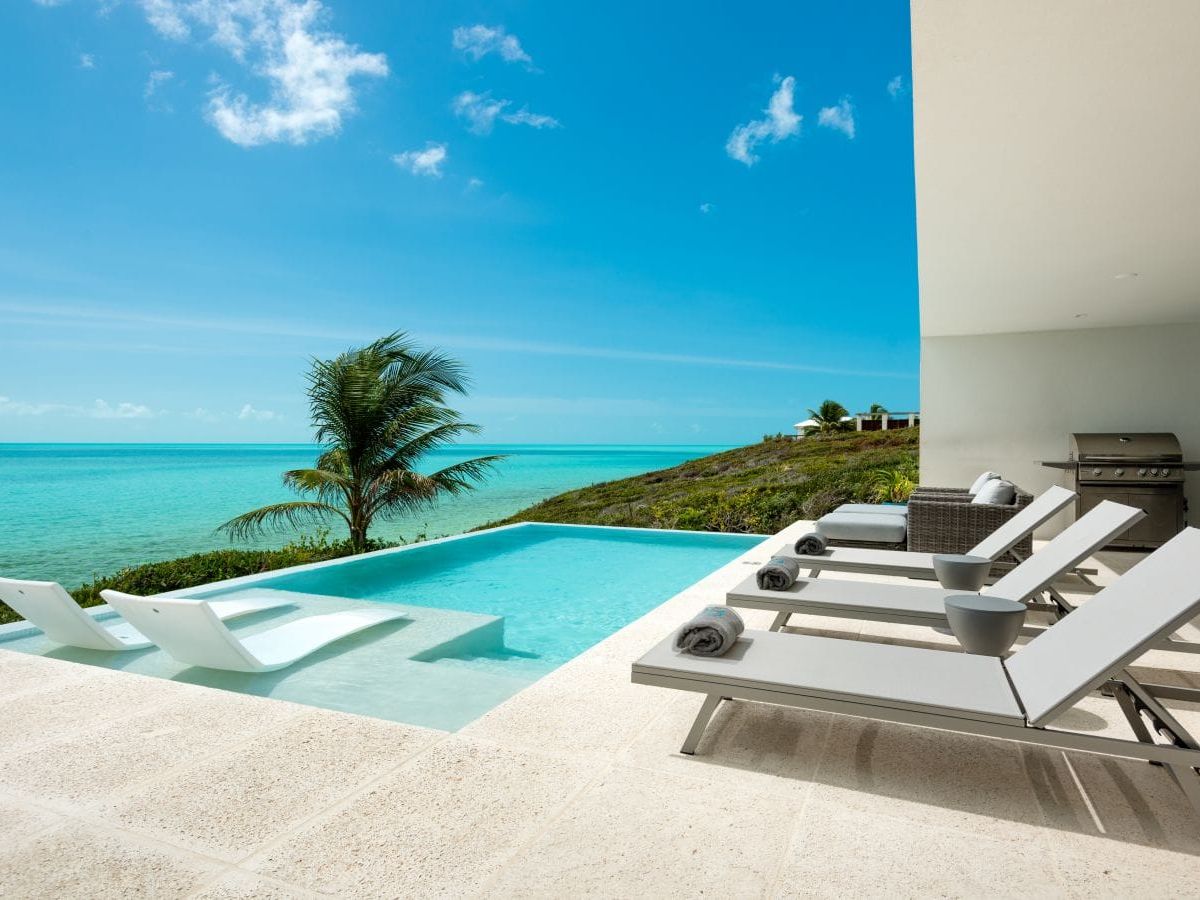 This oceanfront pool deck sits right above bright turquoise water, offering a quiet and dreamy place to relax under the sun. Sleek loungers and a modern design make the space feel clean, calm, and luxurious. It’s the kind of vacation spot that feels almost unreal in how beautiful and peaceful it is.