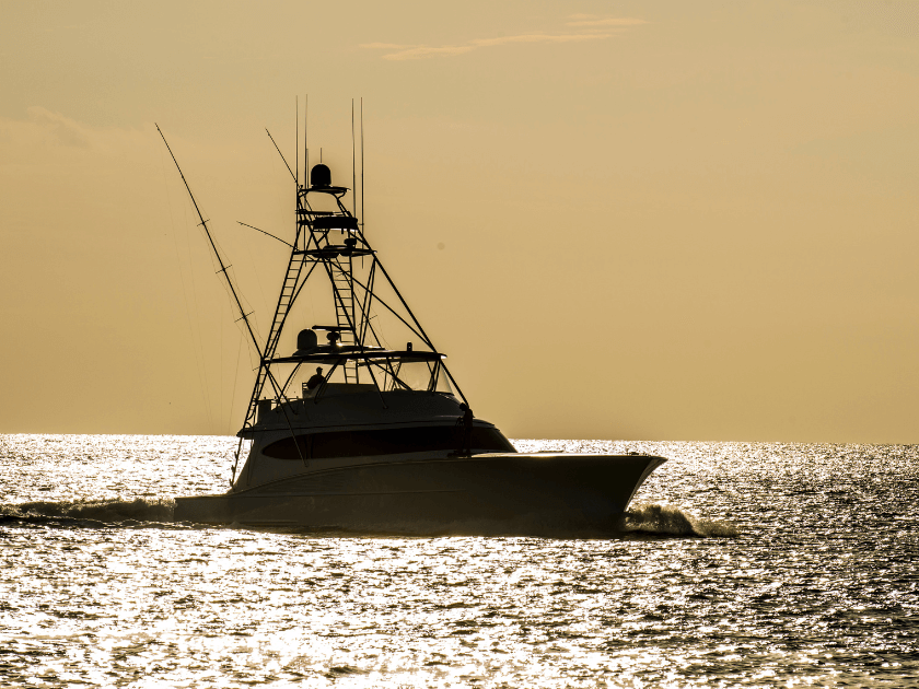 A charter fishing boat cruises across the water under a golden sky at sunset. Fishing in Kiawah Island means expert guides, no planning stress, and the chance to reel in something big.