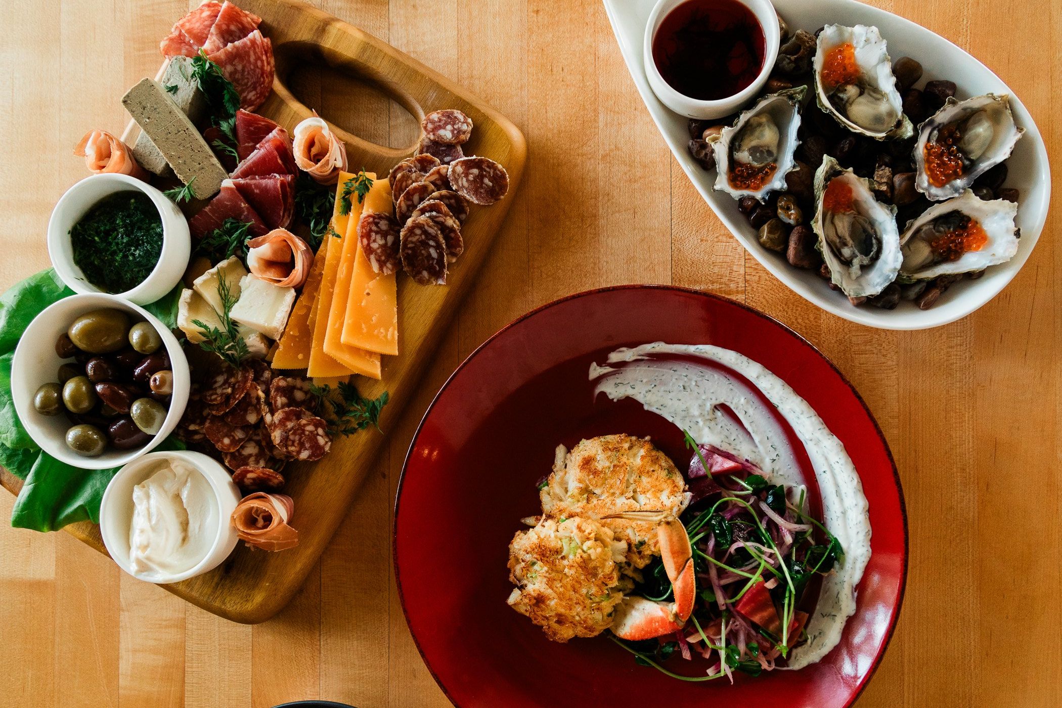 A beautifully plated coastal meal with fresh oysters, a charcuterie board, and a crab cake entrée served on a wooden table in Cannon Beach. This image captures the relaxed yet upscale dining experience you can enjoy while exploring local seafood restaurants near the Oregon coast.