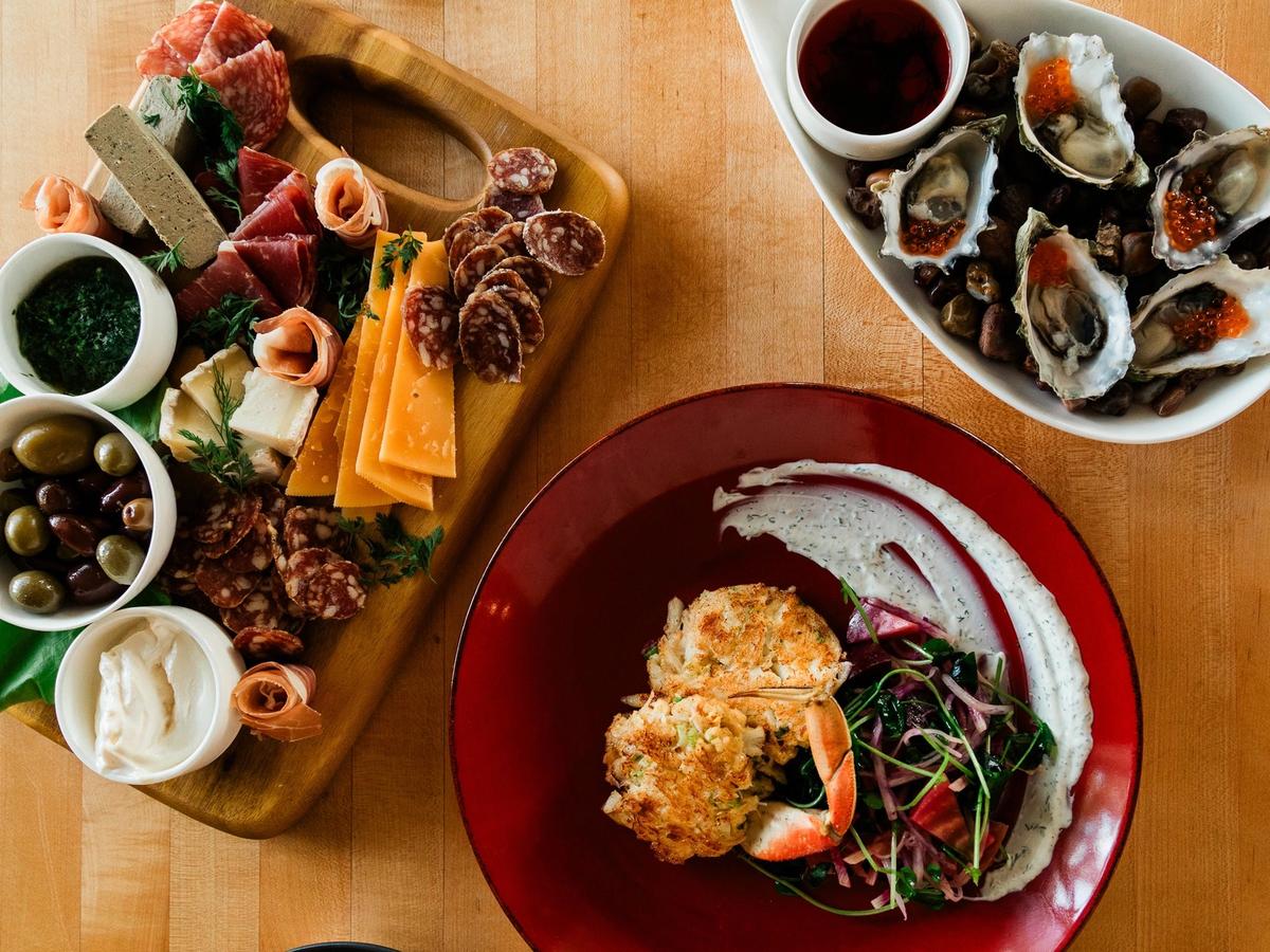 A beautifully plated coastal meal with fresh oysters, a charcuterie board, and a crab cake entrée served on a wooden table in Cannon Beach. This image captures the relaxed yet upscale dining experience you can enjoy while exploring local seafood restaurants near the Oregon coast.