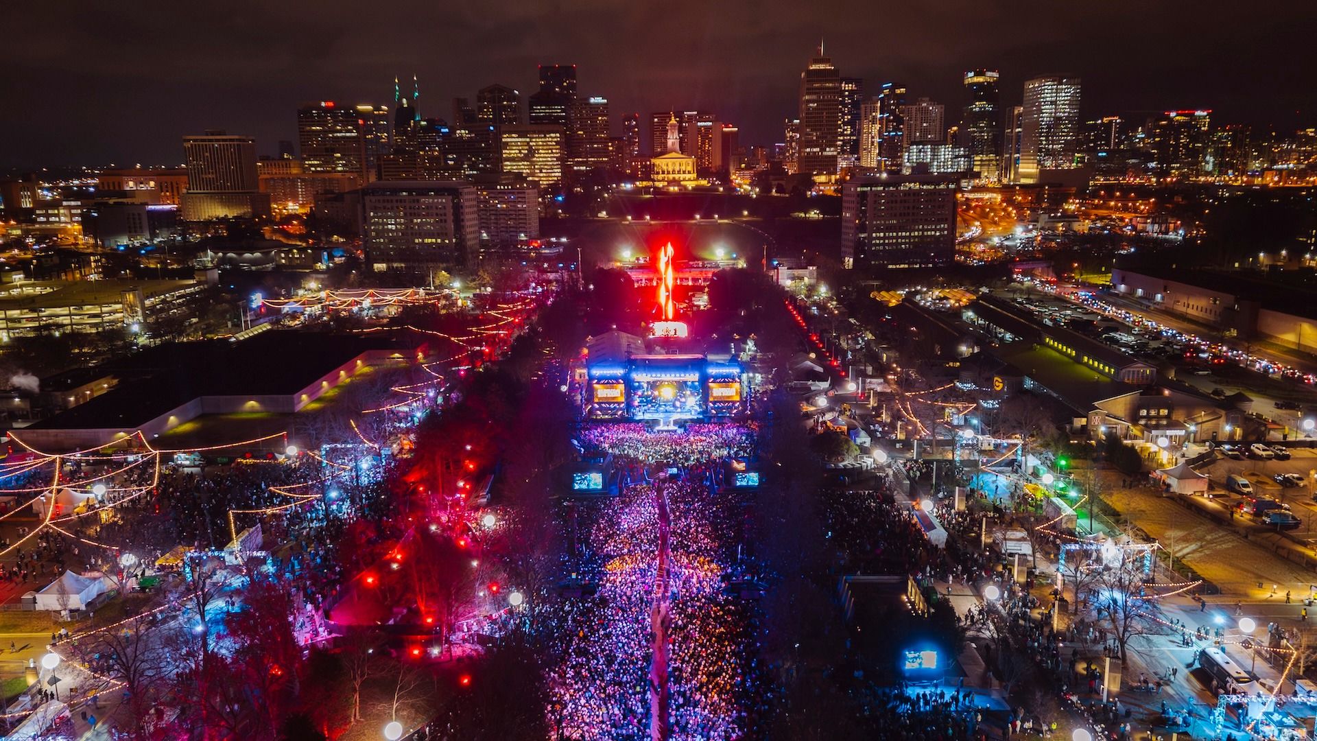 An aerial view of Nashville’s New Year’s Eve Big Bash showing thousands of people packed along Broadway and the main stage. The city skyline glows as live music and lights fill the streets.