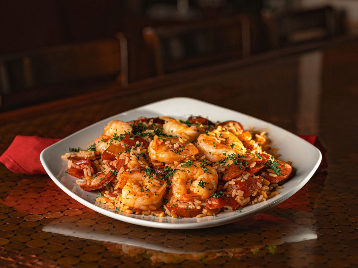 A plate of shrimp and sausage jambalaya garnished with herbs, served over seasoned rice.