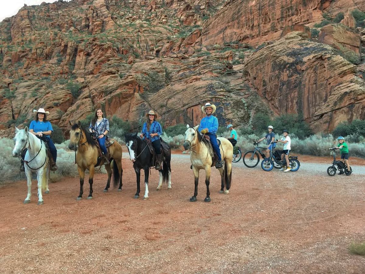 Cyclists ride along a scenic paved trail in Snow Canyon State Park, surrounded by red cliffs and desert landscapes.