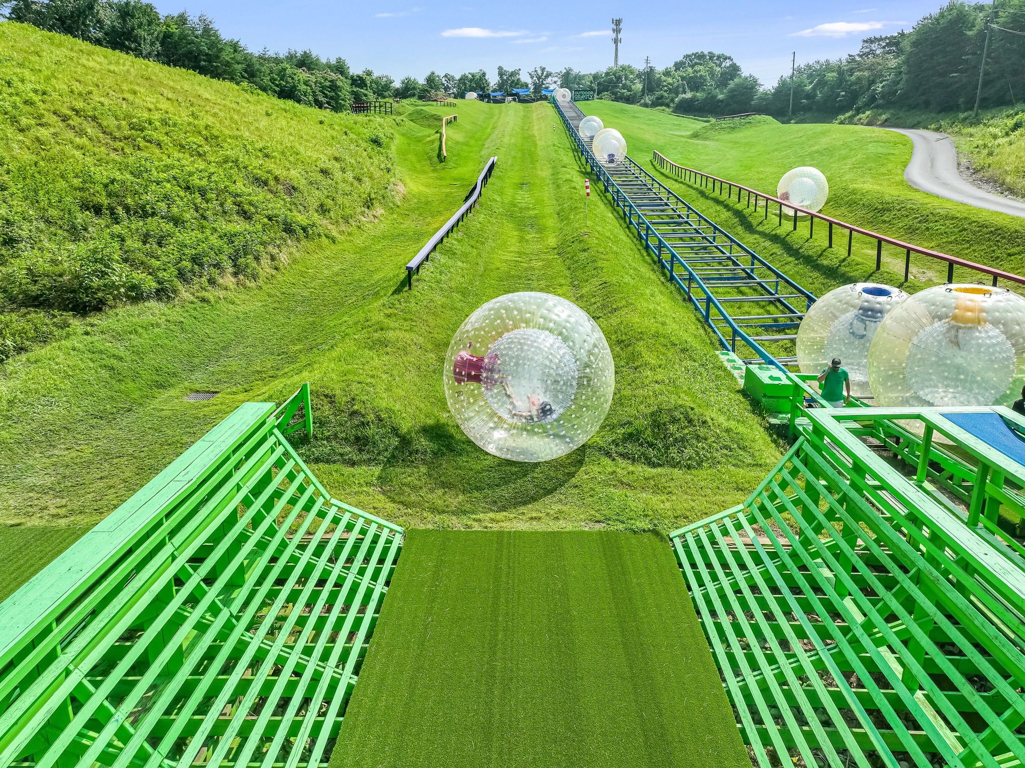Riders roll downhill inside giant inflatable zorbing balls at The Outdoor Gravity Park surrounded by green hills and mountain scenery. This fun Smoky Mountain attraction is a popular outdoor adventure for families, groups, and thrill-seekers visiting the area.