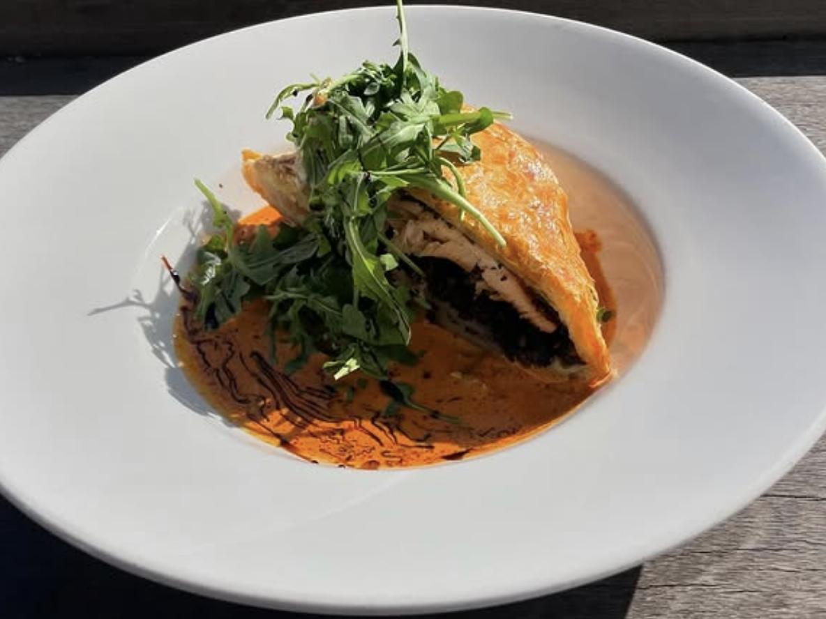Plated chicken Wellington topped with arugula, served over a creamy roasted red pepper sauce with a drizzle of balsamic reduction.