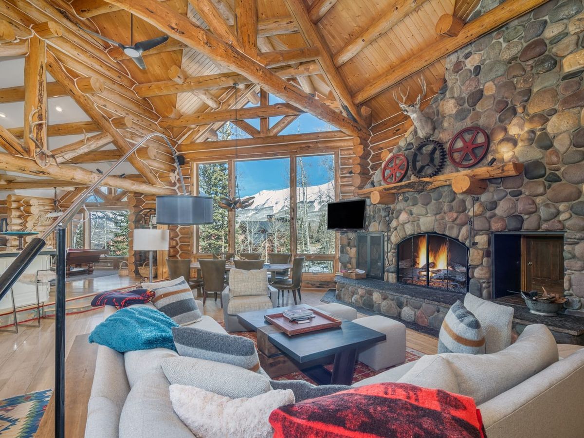 A luxury mountain lodge surrounded by snowy peaks and tall evergreens in Telluride. The home features grand windows, stone and wood design, and cozy interiors perfect for families or groups seeking a true alpine escape.