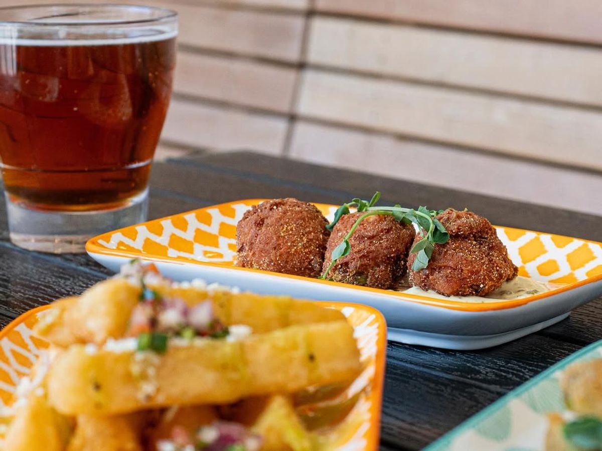 Crispy hush puppies on creamy dipping sauce with fresh herbs and a cold amber beer. A mix of bold flavor and Southern soul in every bite.