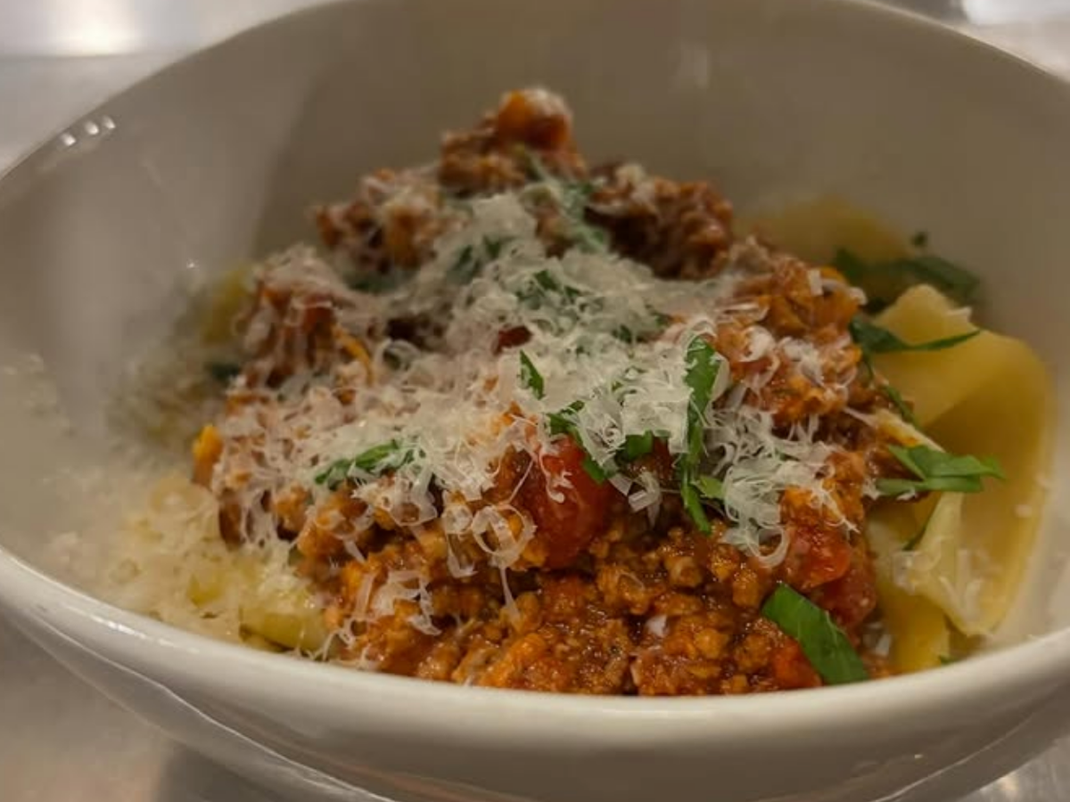Bowl of fresh pappardelle pasta topped with hearty Bolognese sauce, grated Parmesan cheese, and fresh basil.