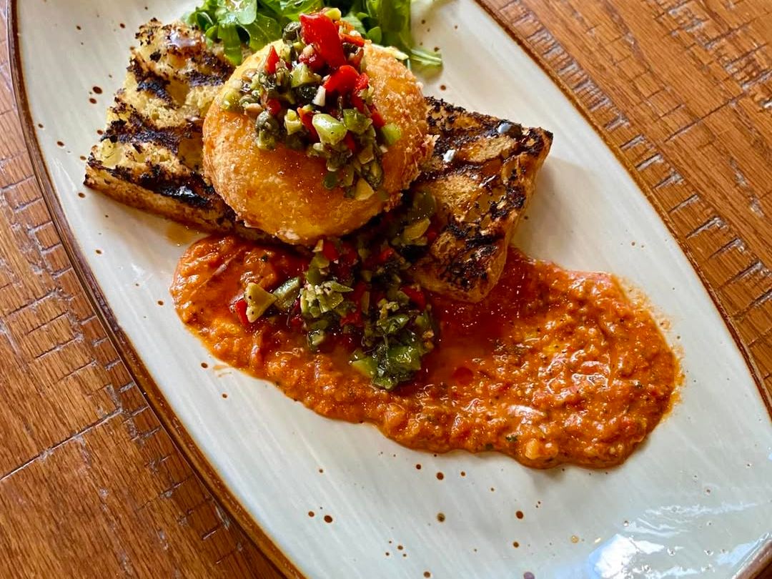 Fried goat cheese stacked on grilled toast with red pepper sauce and olive tapenade. A gourmet starter served with a fresh side salad at a wine-focused eatery.