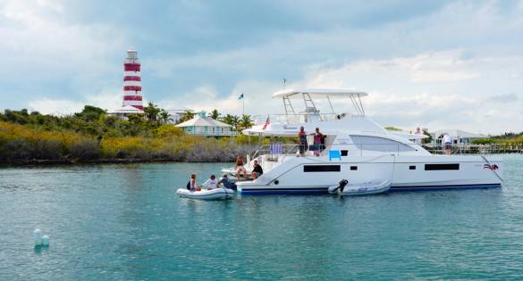 A luxury catamaran anchored in calm Bahamian waters with guests enjoying the day near a lighthouse. Boating and sailing are popular ways to explore hidden beaches and small islands. This scene shows relaxed island cruising at its best.