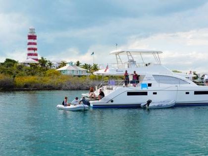 A luxury catamaran anchored in calm Bahamian waters with guests enjoying the day near a lighthouse. Boating and sailing are popular ways to explore hidden beaches and small islands. This scene shows relaxed island cruising at its best.
