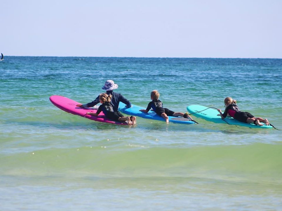 Kids paddle out on colorful surfboards during a beginner surf lesson in the gentle Gulf waves. Guided by an instructor, they learn ocean safety while having fun in the sun.