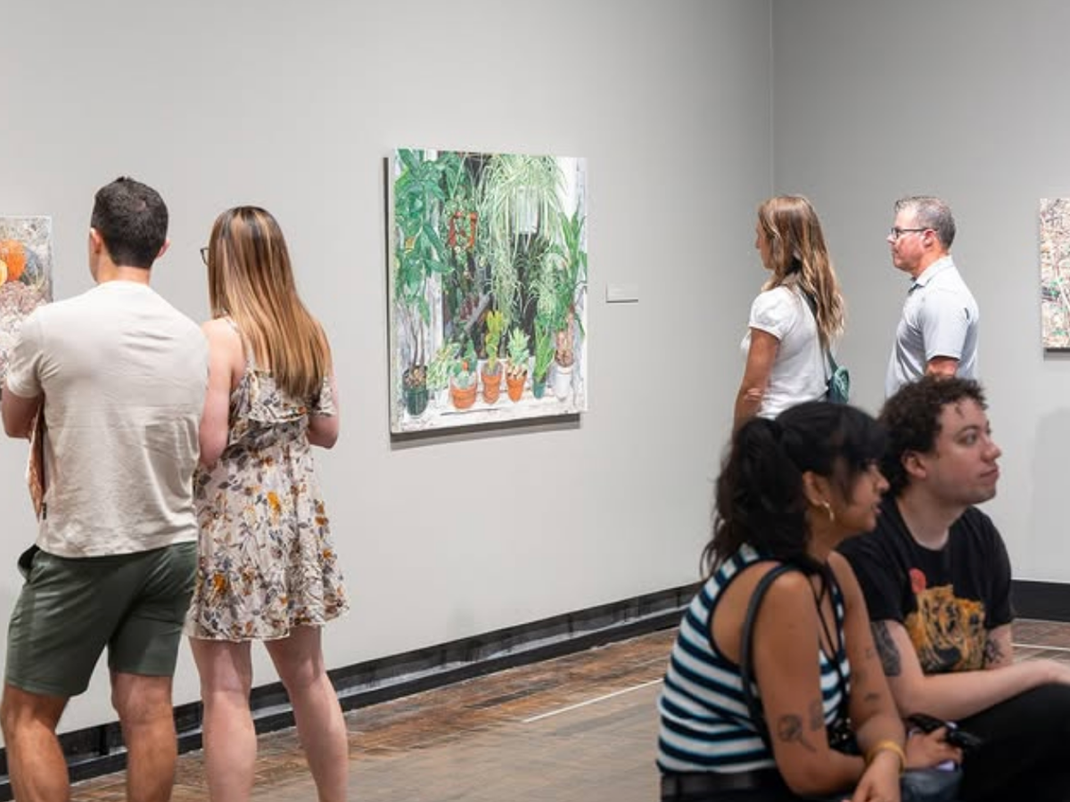 Visitors observe colorful paintings in a modern art gallery while others sit and discuss the exhibits.