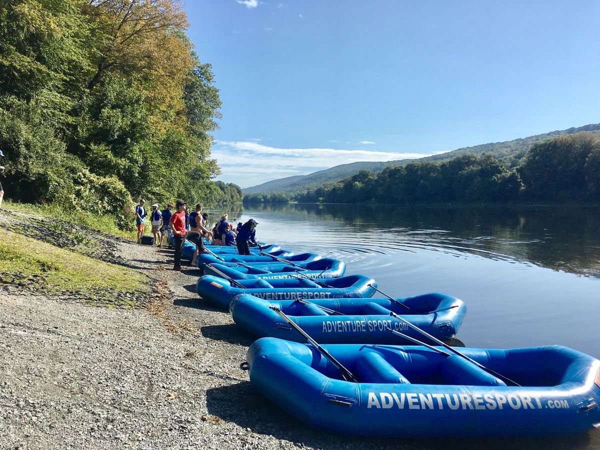 Groups preparing bright blue rafts along a calm river with Pocono mountain views in the background.