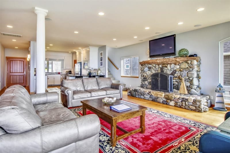 A spacious coastal living room with leather seating, a stone fireplace, and an open layout perfect for group gatherings. This bright interior creates a warm and comfortable space to relax after a day exploring the beach.