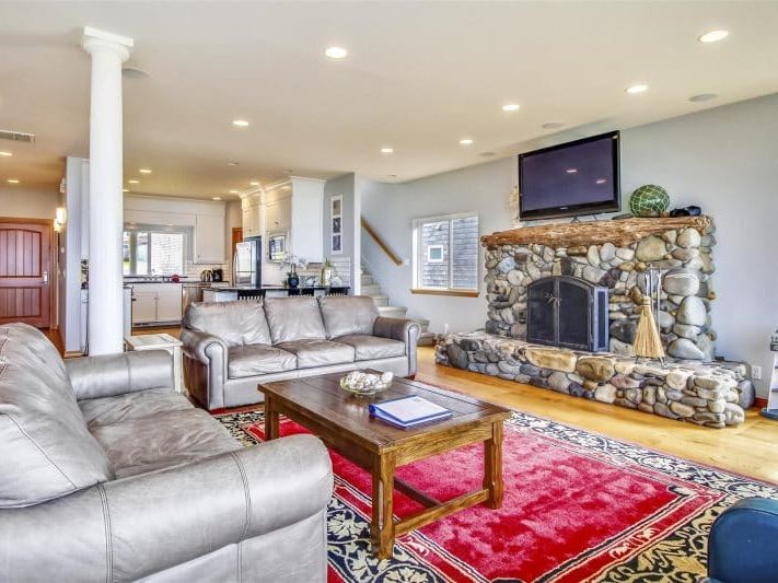 A spacious coastal living room with leather seating, a stone fireplace, and an open layout perfect for group gatherings. This bright interior creates a warm and comfortable space to relax after a day exploring the beach.