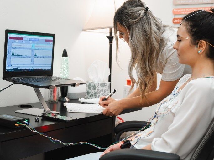 A wellness practitioner records notes while a client undergoes a biofeedback session at Simply Health Collective. The calm setting blends science and holistic care to help balance body and mind.