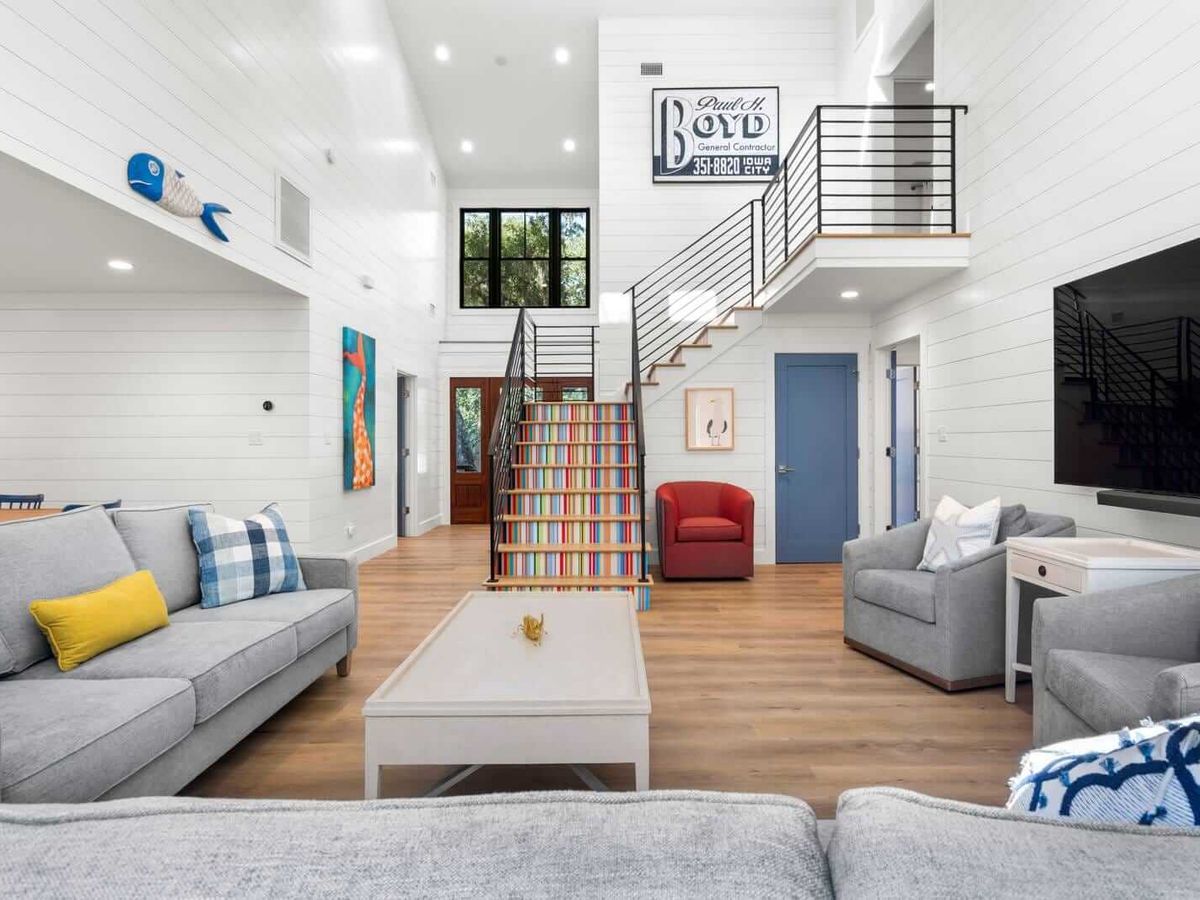 A bright and airy living room with bold colors and clean coastal style. The colorful staircase gives the space a fun, modern twist.