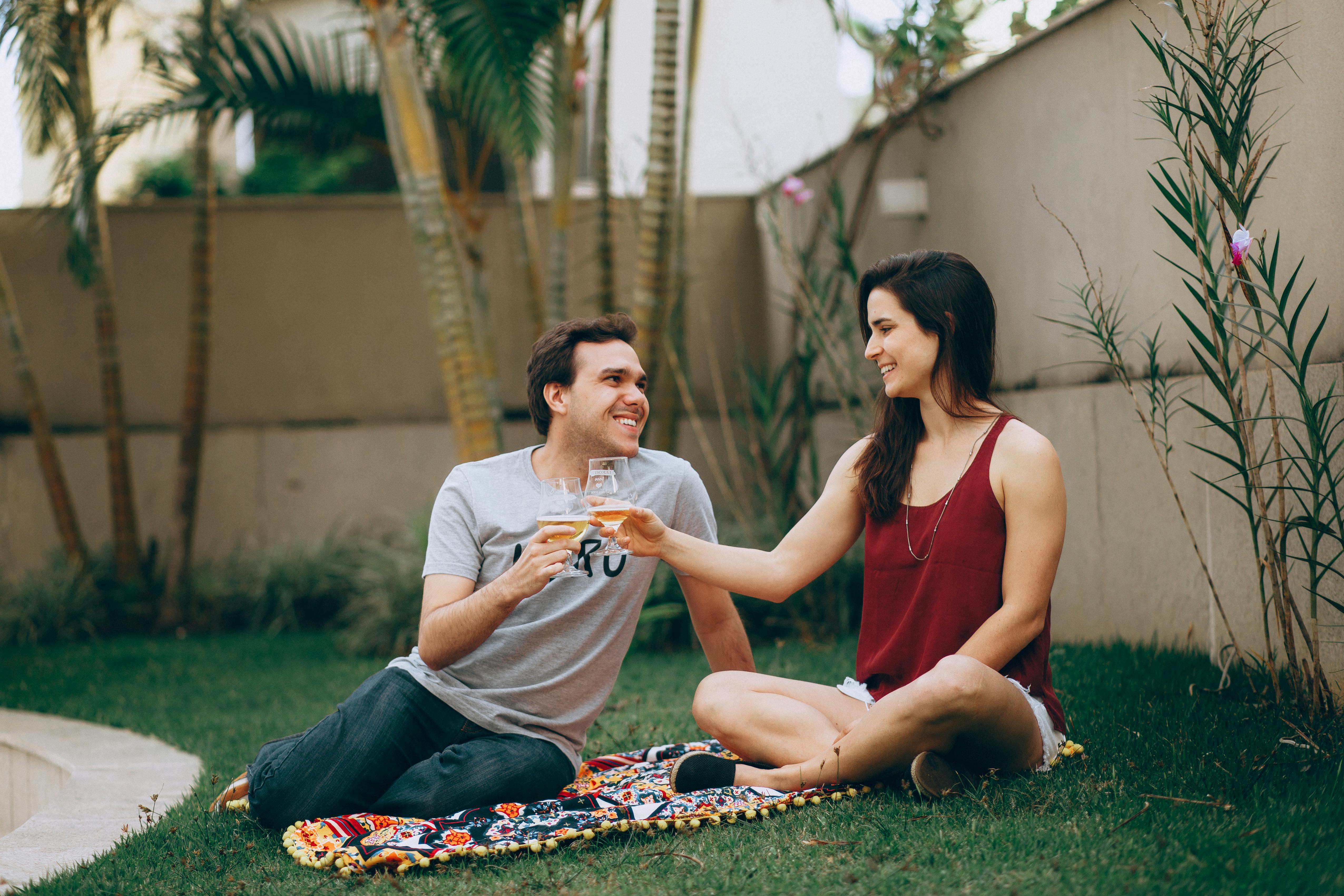 A smiling couple toasts with drinks while sitting on a blanket in a sunny backyard. The relaxed atmosphere reflects the personalized comfort and warmth of a private vacation rental stay.