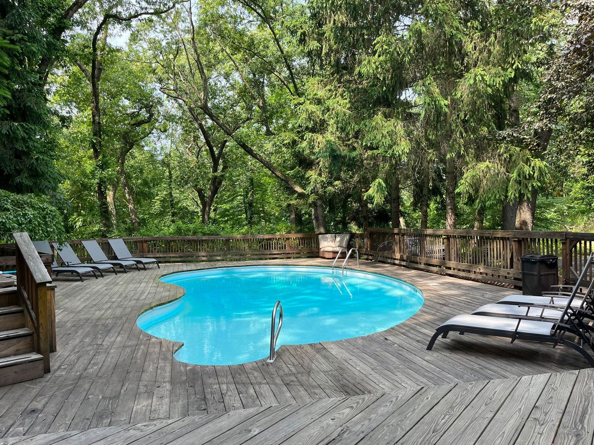 A sparkling blue pool is surrounded by wooden decking and tall trees, offering a peaceful place to relax. Lounge chairs line the poolside, creating a private retreat perfect for sunbathing or afternoon swims.
