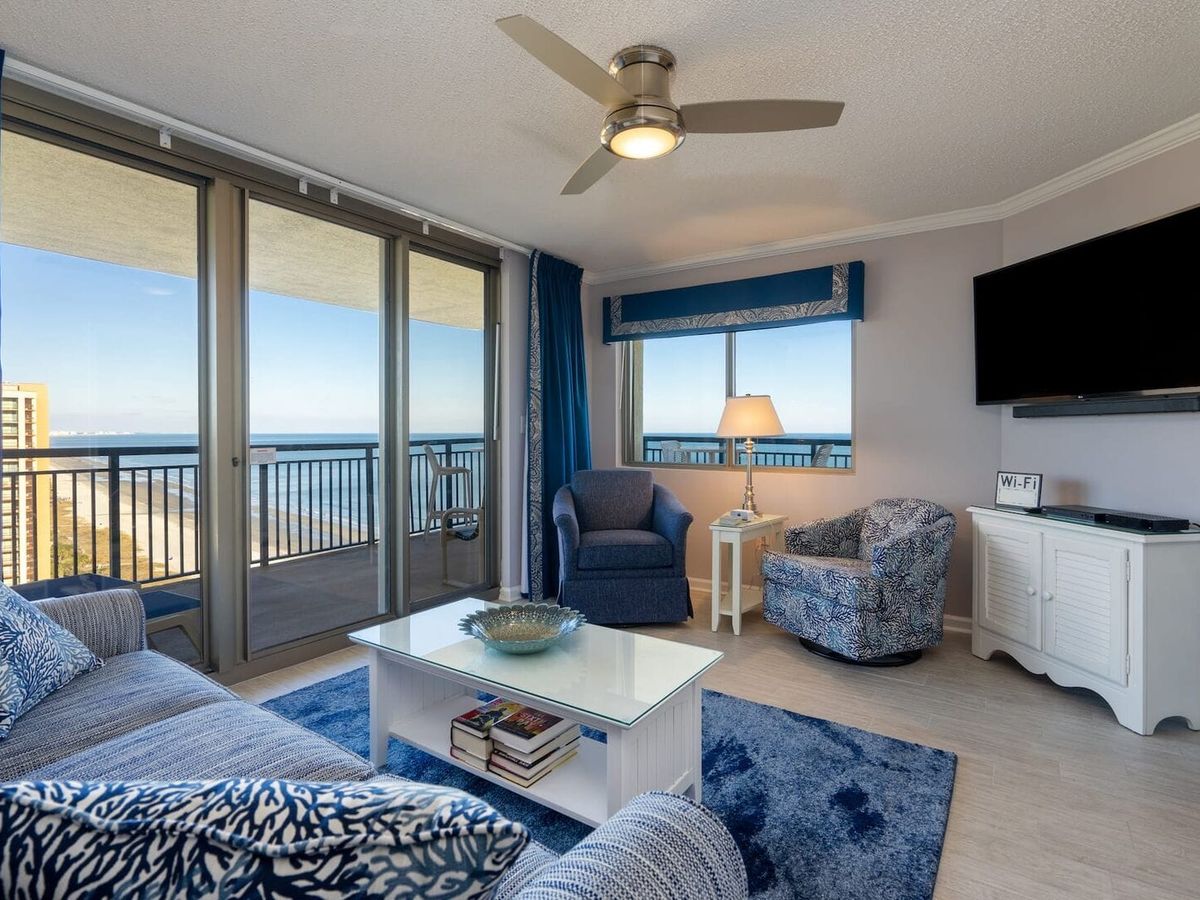 Bright and open living space with cozy blue and yellow accents, huge windows, and an oceanfront balcony that’s perfect for morning coffee. Great for couples or small families looking for a beachside break.