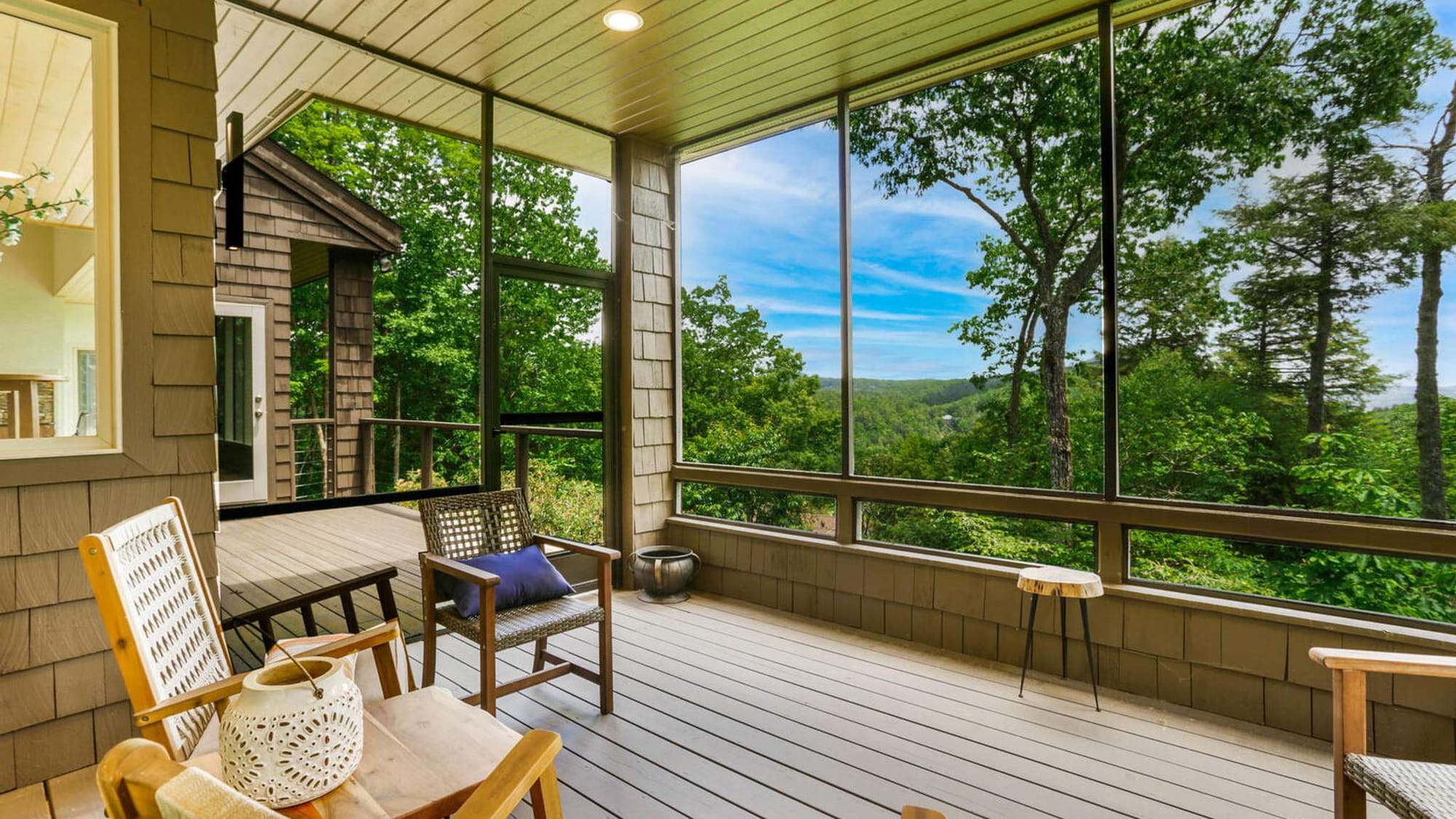 Bright screened porch with comfortable seating and large windows overlooking lush forest and distant mountain views. This relaxing indoor-outdoor space is perfect for morning coffee, reading, or enjoying fresh mountain air.
