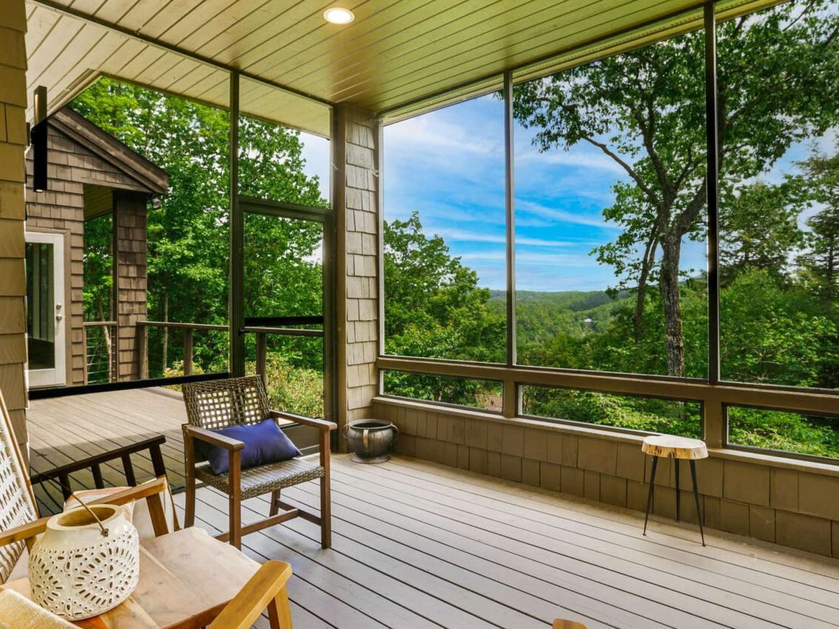 Bright screened porch with comfortable seating and large windows overlooking lush forest and distant mountain views. This relaxing indoor-outdoor space is perfect for morning coffee, reading, or enjoying fresh mountain air.