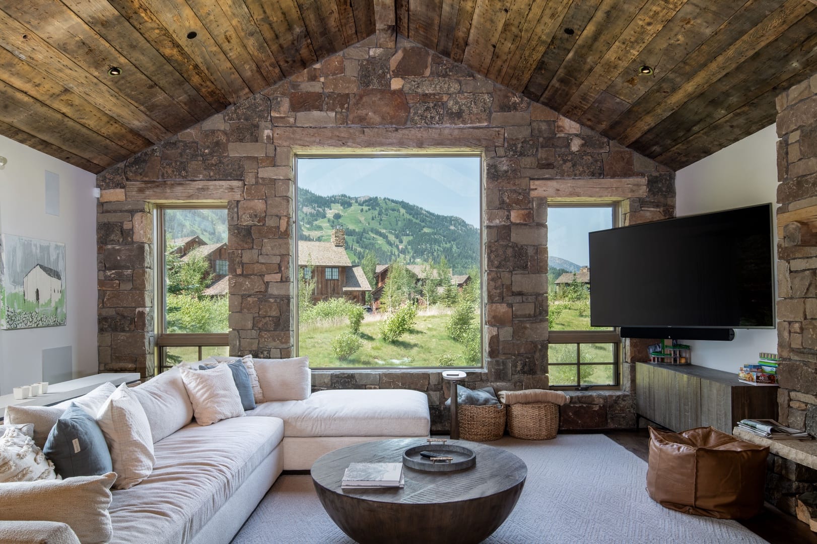 Interior of living room with flat-screen TV and open windows on stone accent wall overlooking mountain views